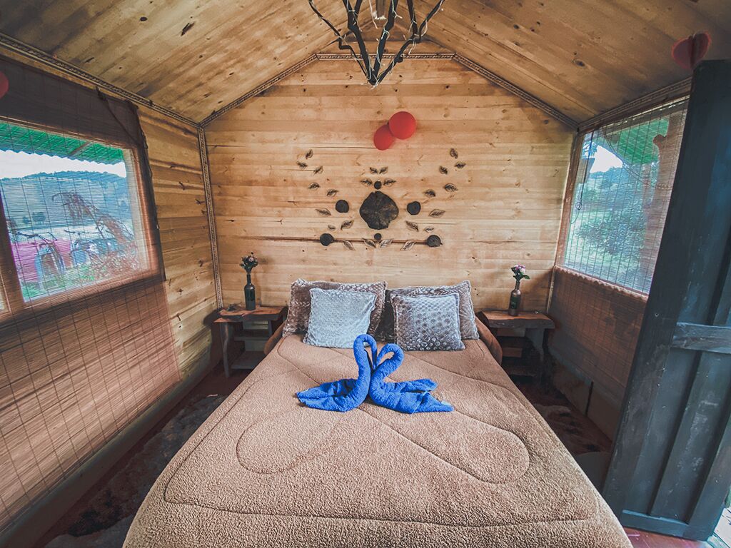 A cozy wooden cabin room with a bed, pillows, a decorative swan towel, and a rustic ceiling.
