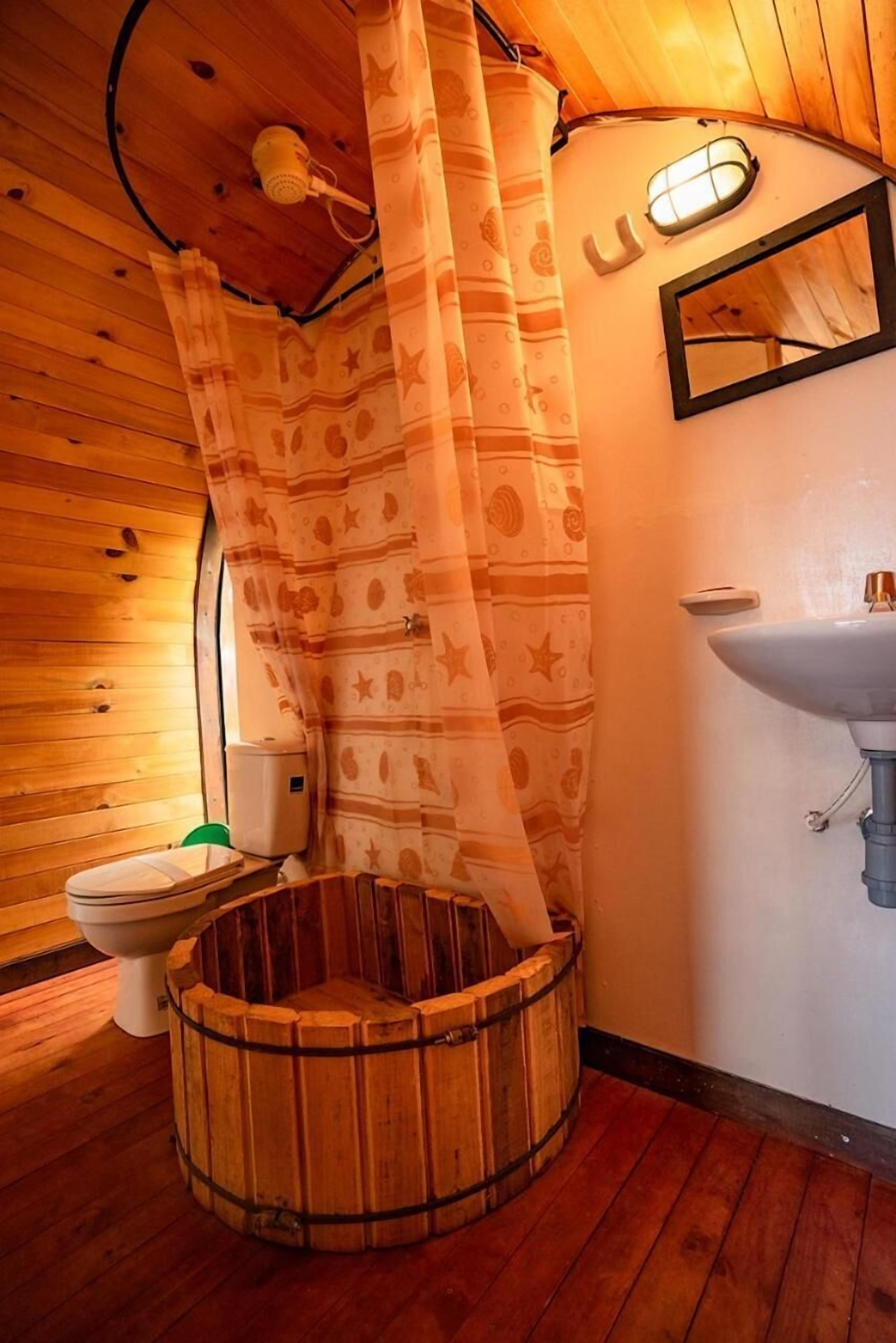 Een houten badkamer met een houten bad, toilet en wastafel.