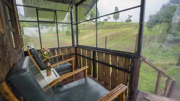 Una habitación acogedora con un banco de madera, una mesa con un jarrón de flores y vistas a un paisaje con césped a través de amplios ventanales.