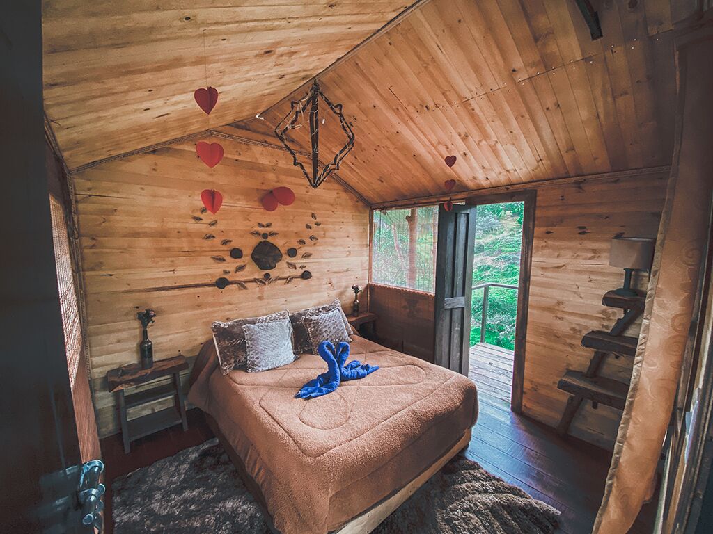 A cozy wooden cabin bedroom with a bed, pillows, a small table, and a hanging light fixture.