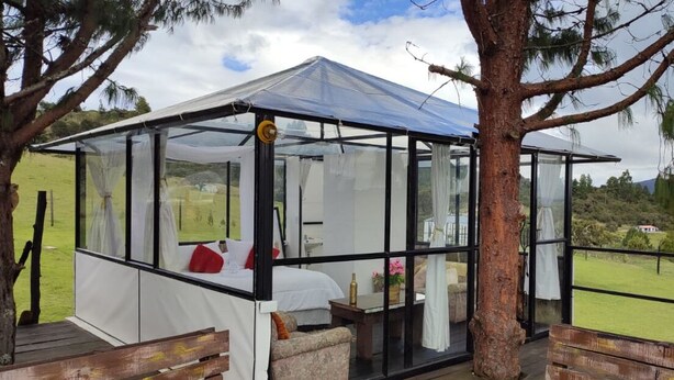 A glass-roofed structure with a bed, a small table, and a bench. - Tu Glamping (Chocontá)