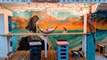 A tiki bar with a wooden deck, a mural with a sunset and sea theme, and a sign above the bar.