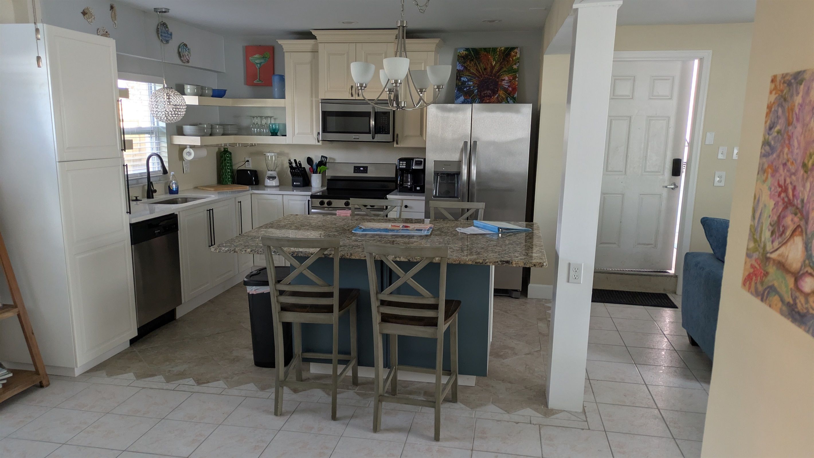 A kitchen with white cabinets, a central island with bar stools, a microwave, a refrigerator, and a sink.