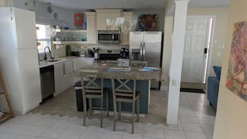A kitchen with white cabinets, a central island with bar stools, a microwave, a refrigerator, and a sink.