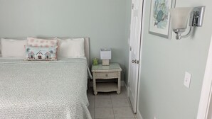 Un dormitorio con cama, almohadas, una mesita de noche con lámpara y una puerta.