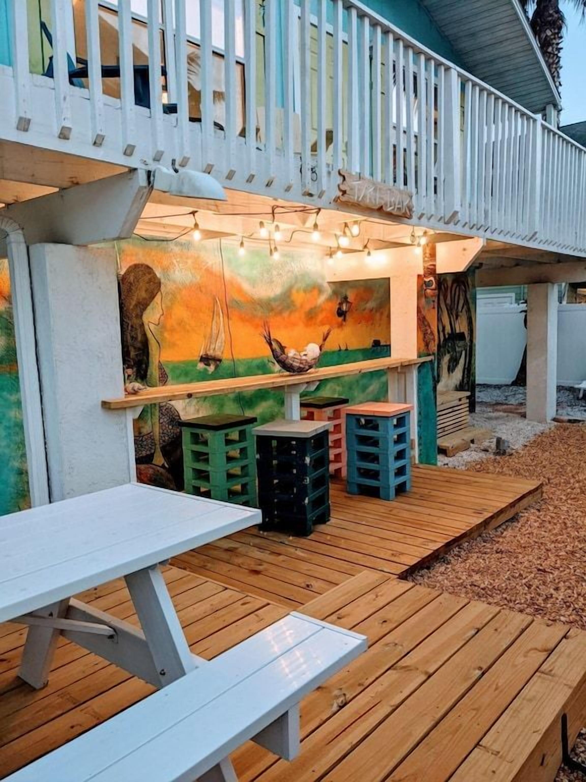 Une terrasse extérieure avec une plateforme en bois, une table blanche et des tabourets colorés.