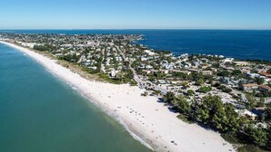 Vista aérea de un pueblo costero con una playa de arena extensa, zona residencial densa y aguas azules cristalinas.