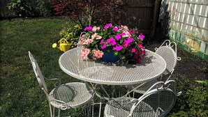 A round metal table with four chairs, surrounded by a garden with various plants and a wooden fence in the background. - Downtown Lebanon, Near Kings Island, Lovely Historic Home, 1st Flr, Washer/Dryer (Lebanon)