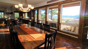 Un vaste espace dédié à la salle à manger, avec une longue table et des chaises en bois, de grandes fenêtres offrant une vue sur l’extérieur, et une enseigne accueillante placée au-dessus des fenêtres.