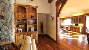 Un vaste espace de vie agrémenté d’une bibliothèque en bois, d’un mur en pierre et offrant une vue sur la cuisine.