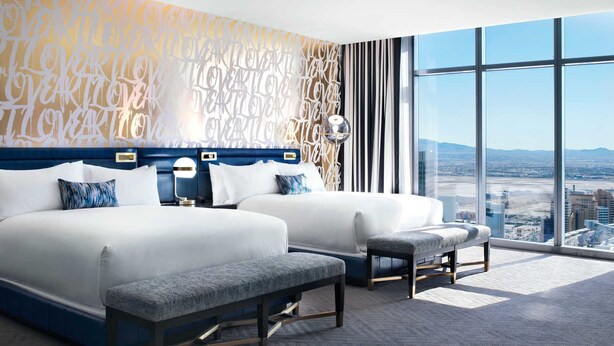 Ein Hotelzimmer mit zwei Betten, einem großen Fenster mit Blick auf die Stadt und einer dekorativen Wand.