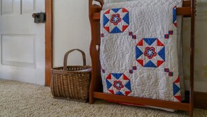 Una silla de madera con un colcha sobre ella, una cesta de mimbre y una puerta al fondo.