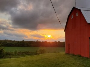 A red barn with a sloped roof, surrounded by a grassy field and trees. - The Weber Farm - Enjoy a beautiful 100 acre farm! (Frohna)