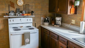 Una cocina con estufa blanca, armarios de madera, un reloj y una cafetera.