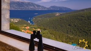 Ein Fenster mit Fernglas, das eine Küstenlandschaft mit Bergen und einem Gewässer zeigt.