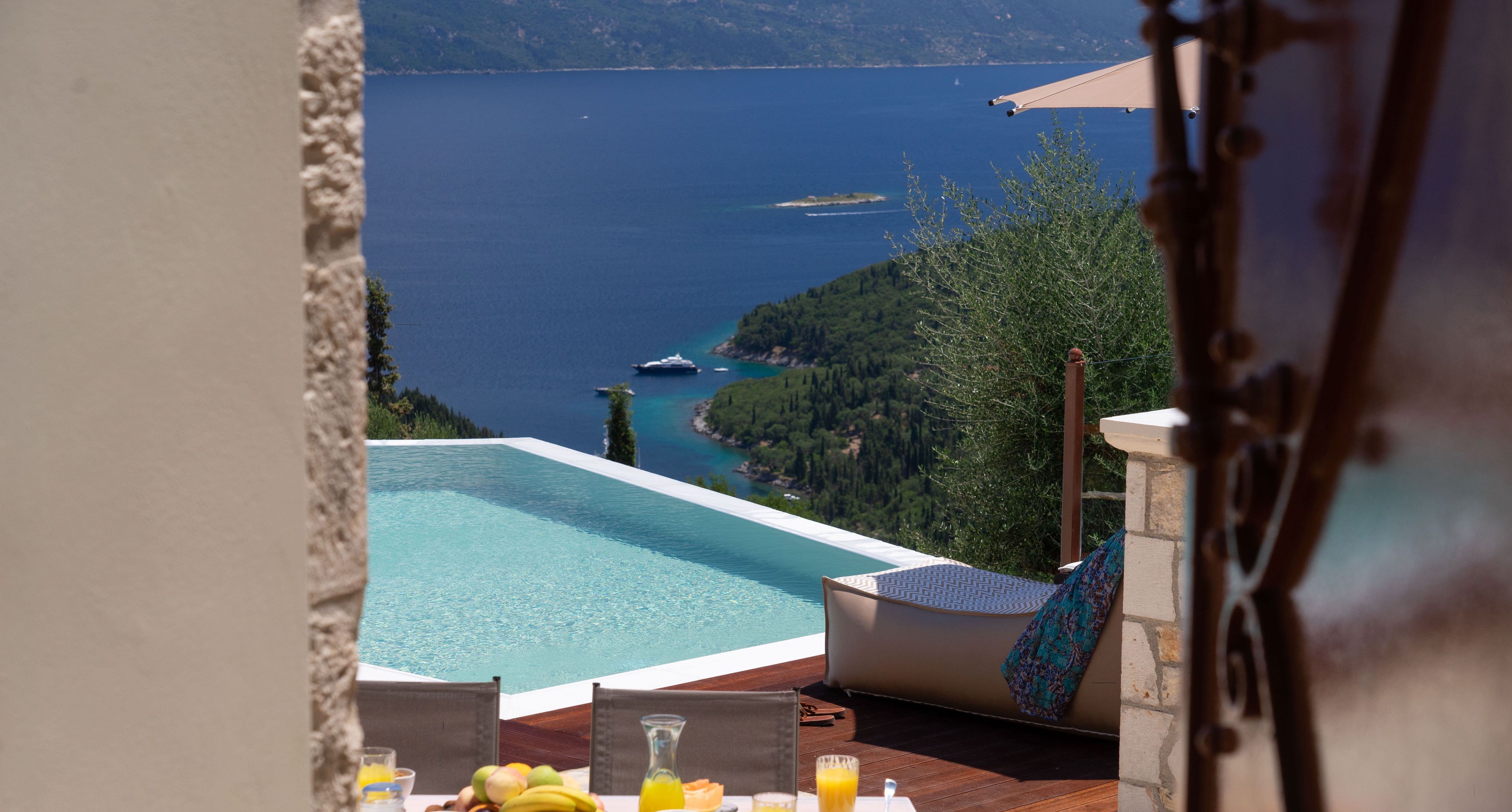 A dining table with breakfast items and a view of a swimming pool and sea.