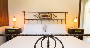 Een bed met een metalen hoofdbord, twee nachtkastjes met lampen en een wandklok.