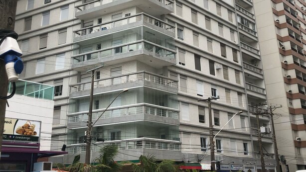 A multi-story building with balconies, a street in front, and parked cars.