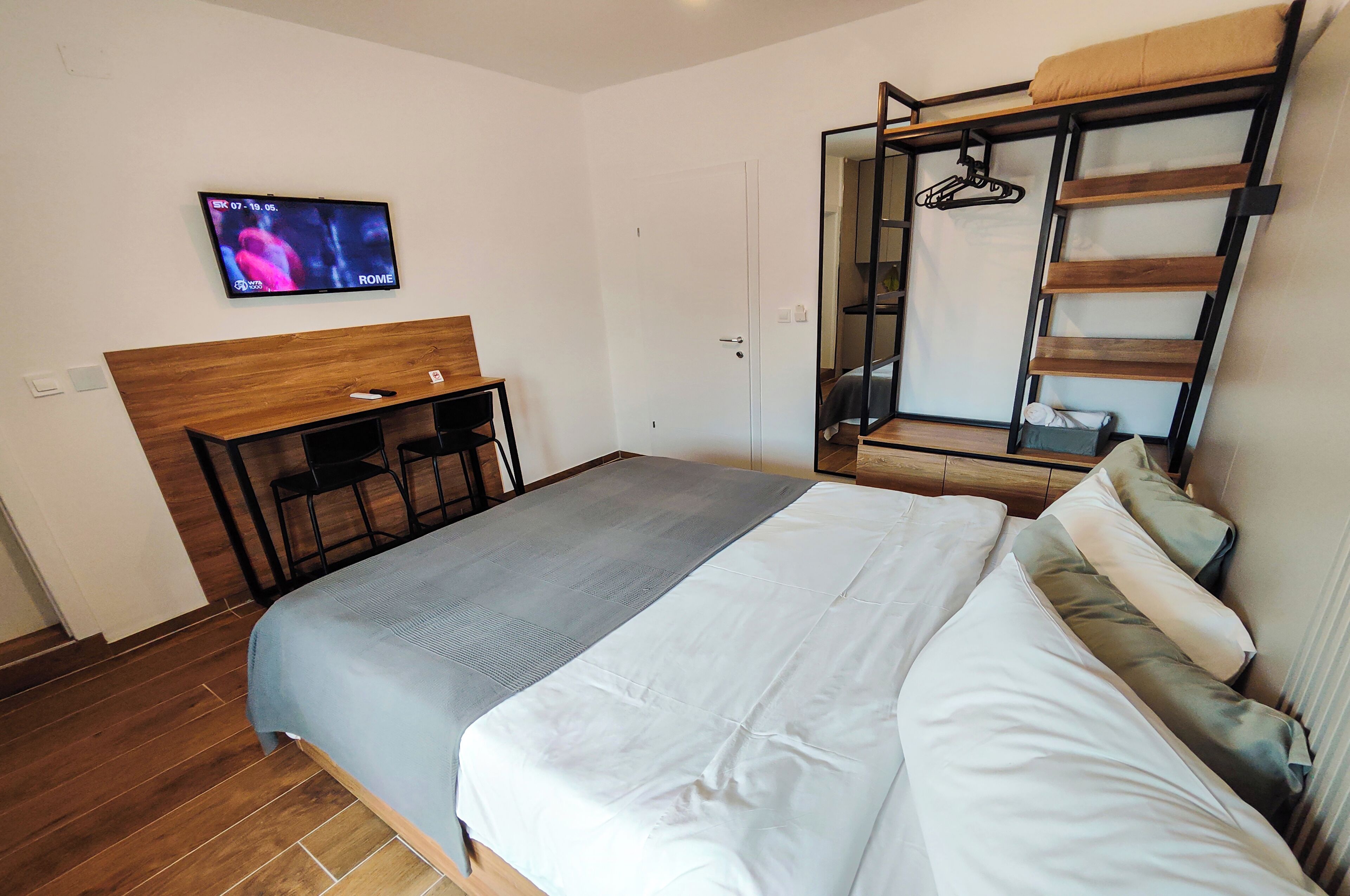 Un dormitorio con cama, escritorio y televisor montado en la pared.
