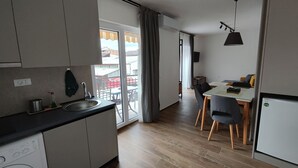 Et moderne køkken med en indbygget vaskemaskine, et spiseområde med bord og stole, og udsigt til det frie gennem et stort vindue.