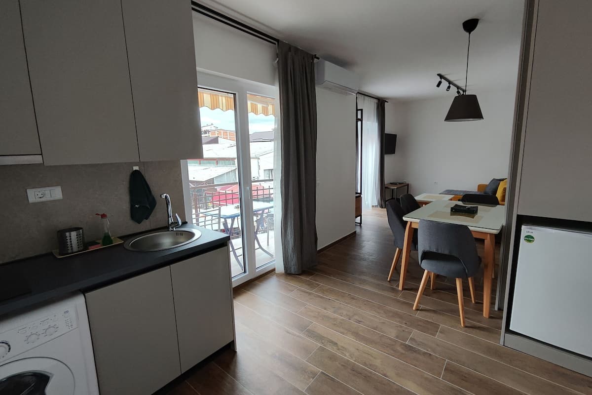 Eine moderne Küche mit integriertem Waschmaschinenanschluss, einem Essbereich mit Tisch und Stühlen sowie Blick ins Freie durch ein großes Fenster.