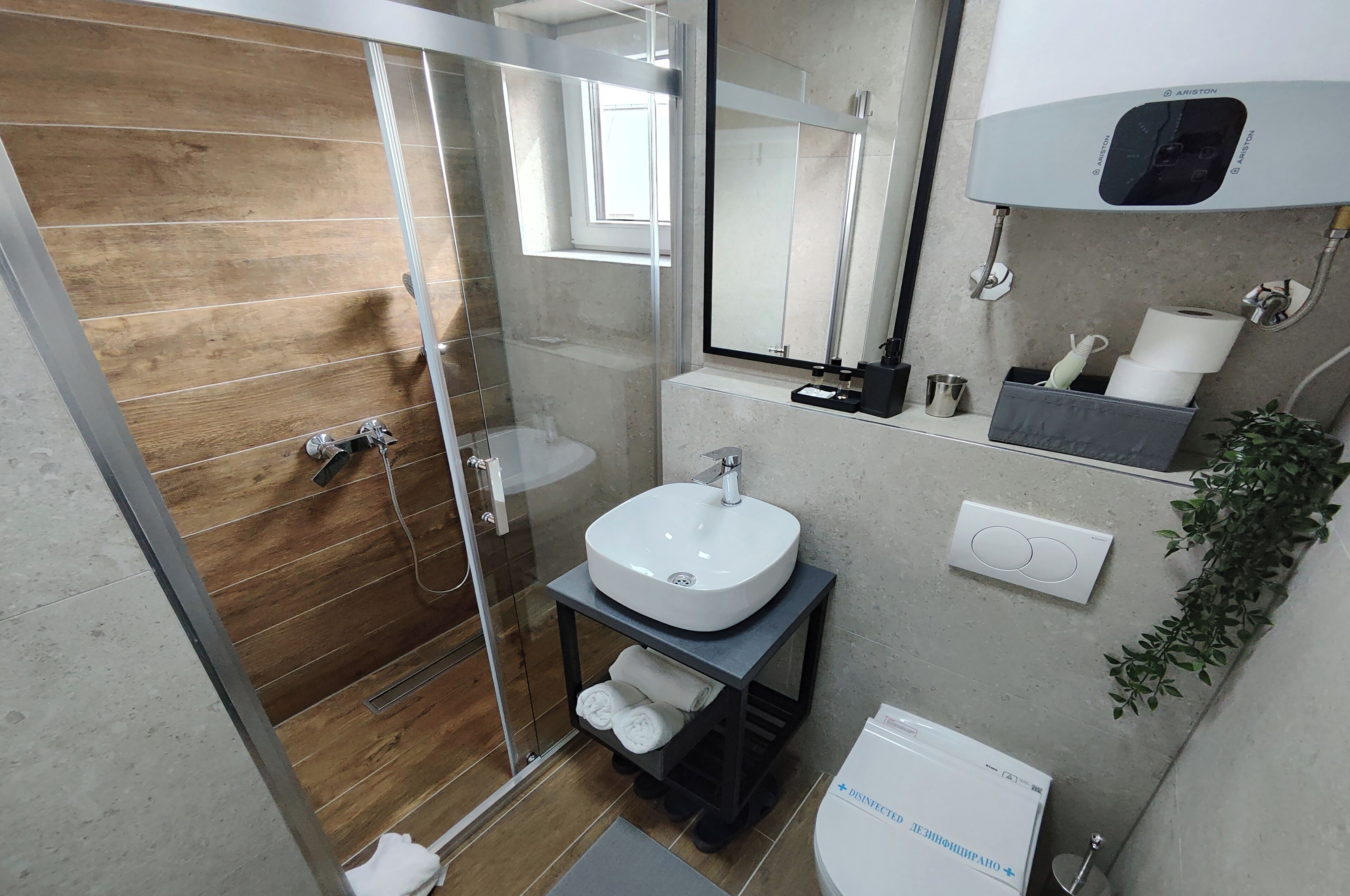 A modern bathroom with a glass shower enclosure, a white sink on a black vanity, a mirror, a heater, and a small plant.