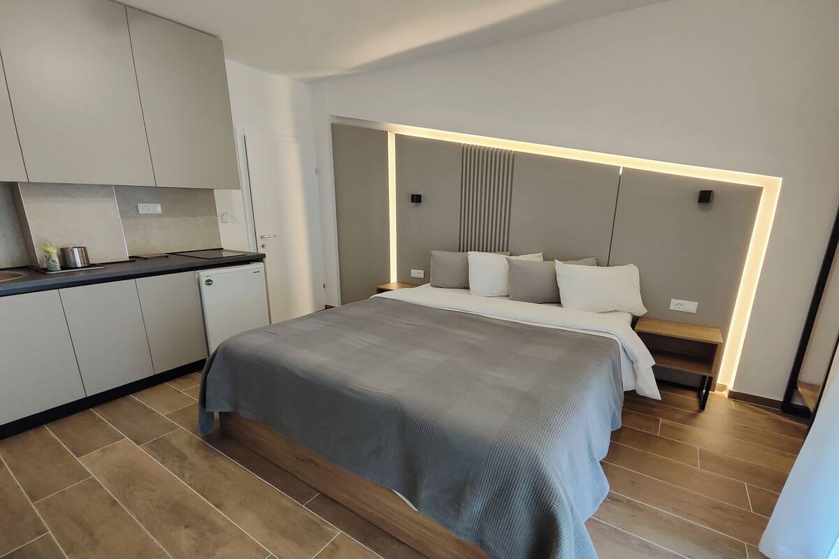 Ein modernes Hotelzimmer mit einem großen Bett, einem Nachttisch, einer integrierten Sitzbank und einer Küchenzeile.