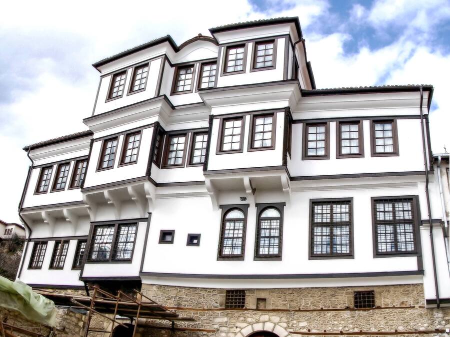 A multi-story building with white walls and dark trim, featuring multiple windows and a stone base.