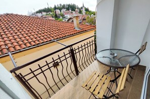 A balcony with a tiled roof, a glass table with chairs, and a view of a town with buildings and a church. - Apartments LAVO (Ohrid)
