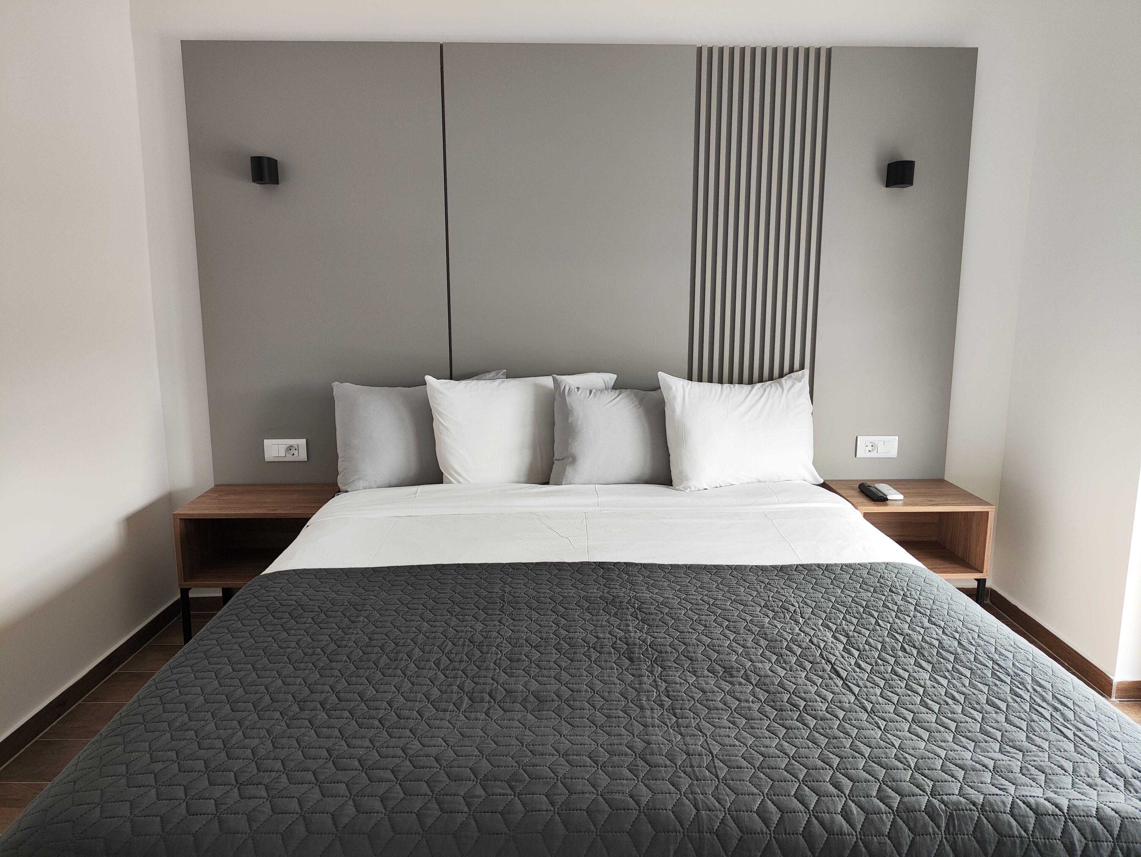 Une chambre d’hôtel moderne avec un grand lit, une table de chevet en bois et une tête de lit ornée de lignes verticales.