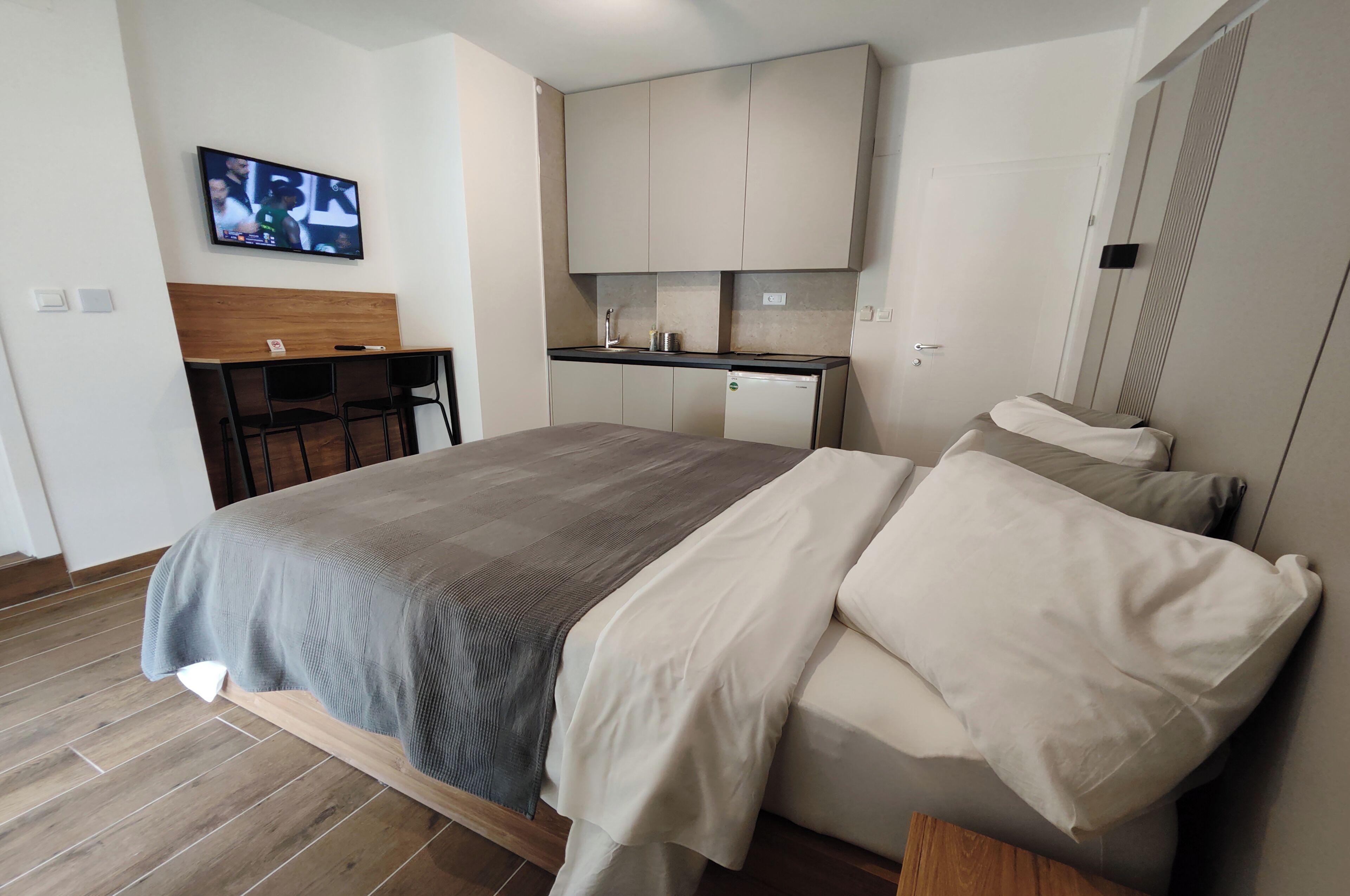 A bedroom with a bed, a TV, a kitchenette, and a dining area.