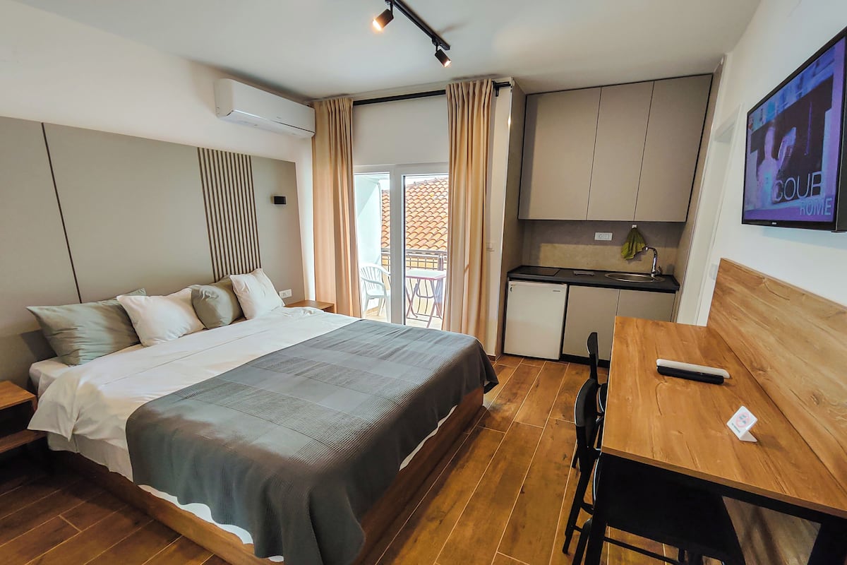 Ein Hotelzimmer mit einem Bett, einem Holztisch, einem Fernseher und einer Küchenzeile.