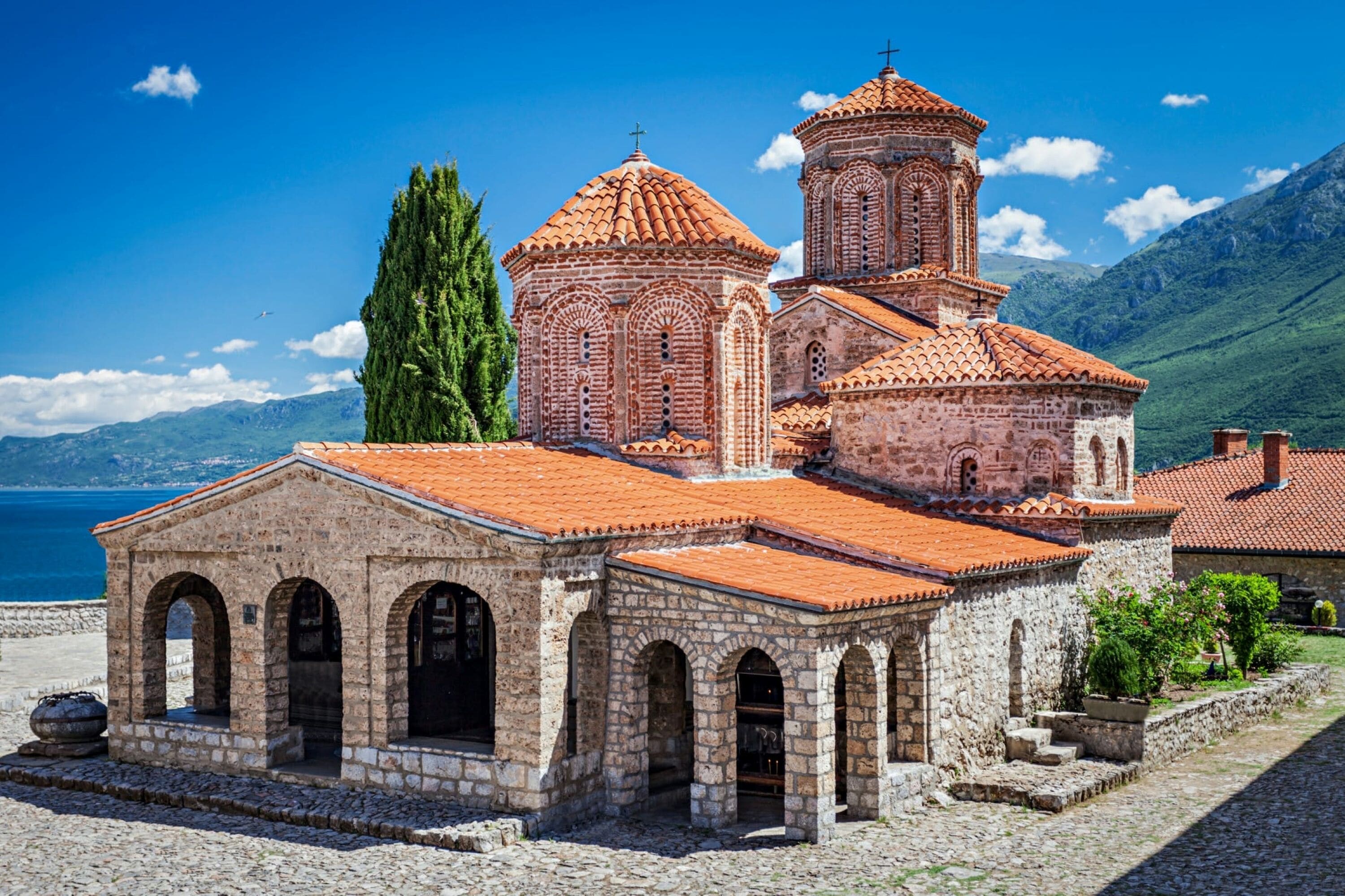 A historic stone church with a red-tiled roof, arched windows, and a bell tower.