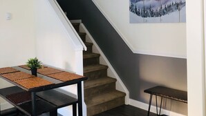 A modern interior with a staircase, a dining table with a plant, and a painting of a mountain landscape.
