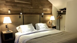 A neatly made bed with two bedside lamps, a wooden headboard, and a small nightstand with a lamp.