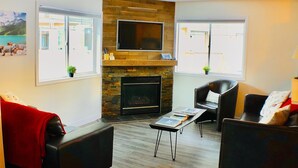 A living room with a fireplace, two leather sofas, a coffee table, and a flat-screen TV mounted on the wall.