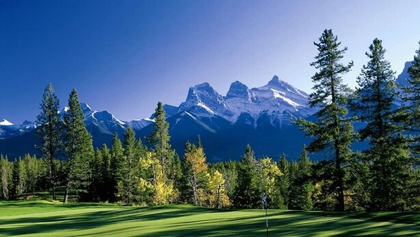 A golf course with a backdrop of snow-capped mountains and a clear blue sky.
