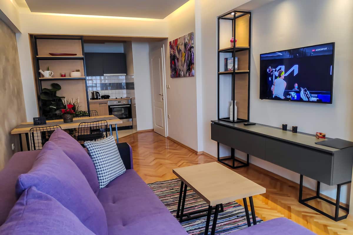 Una sala de estar moderna con un sofá morado, una pequeña mesa de centro y un televisor montado en la pared.