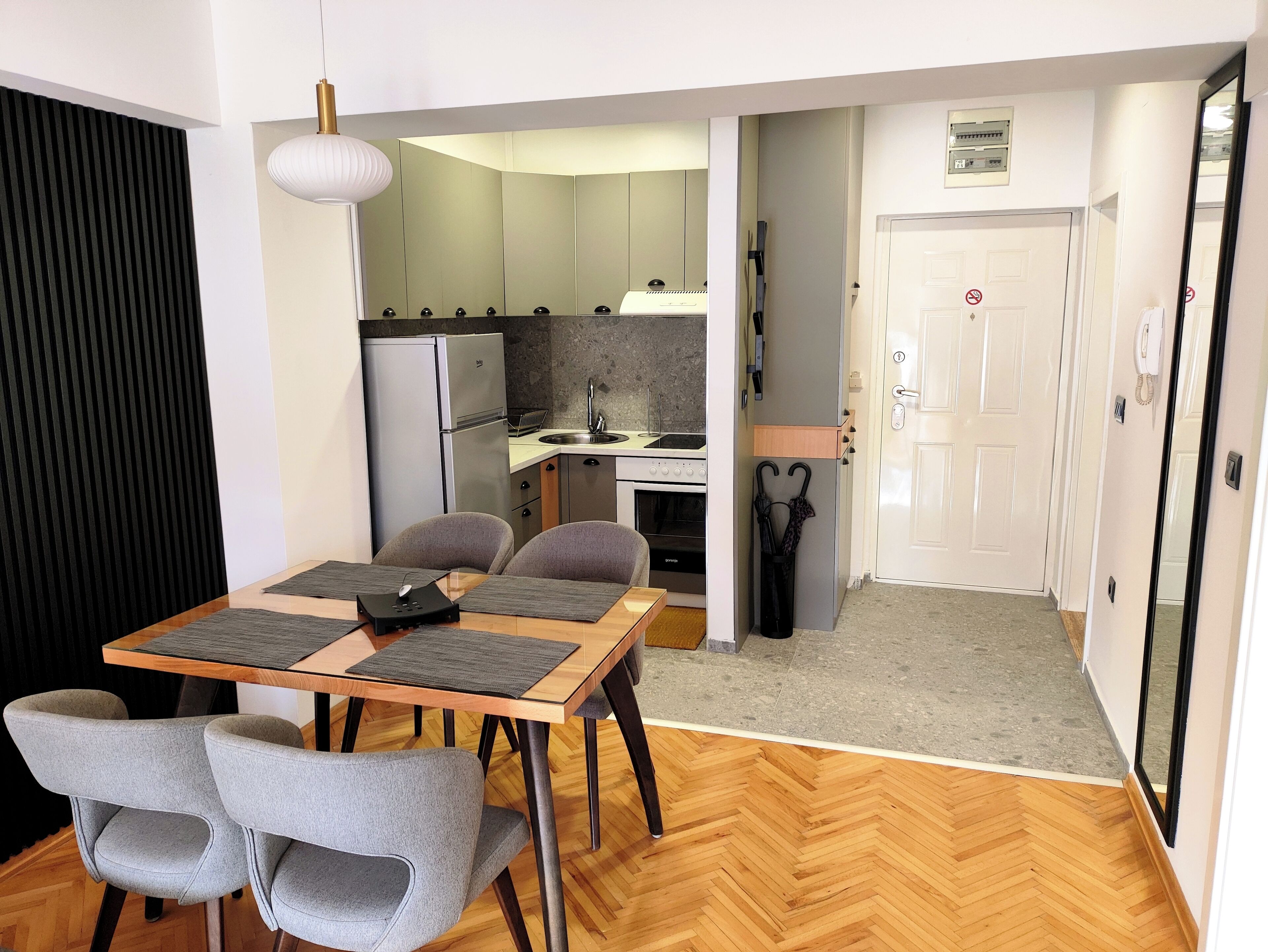 Een kleine leefruimte met een eethoek, kitchenette en een deur naar een gang.