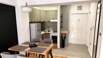 Een kleine leefruimte met een eethoek, kitchenette en een deur naar een gang.
