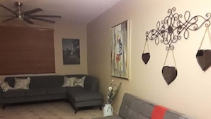 Una sala de estar con dos sofás, un ventilador de techo, obras de arte en la pared y adornos decorativos.