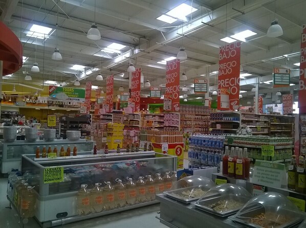 Un supermercado con varios pasillos repletos de productos, carteles promocionales y una sección refrigerada con bebidas.