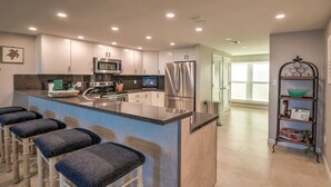 Una cocina moderna con una isla central, taburetes de bar, electrodomésticos de acero inoxidable y una estantería metálica decorativa.