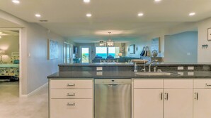 Una cocina moderna con lavavajillas, armarios blancos y vista al área de estar.