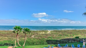 Vista de playa con palmeras, un camino y sillas de descanso azules.
