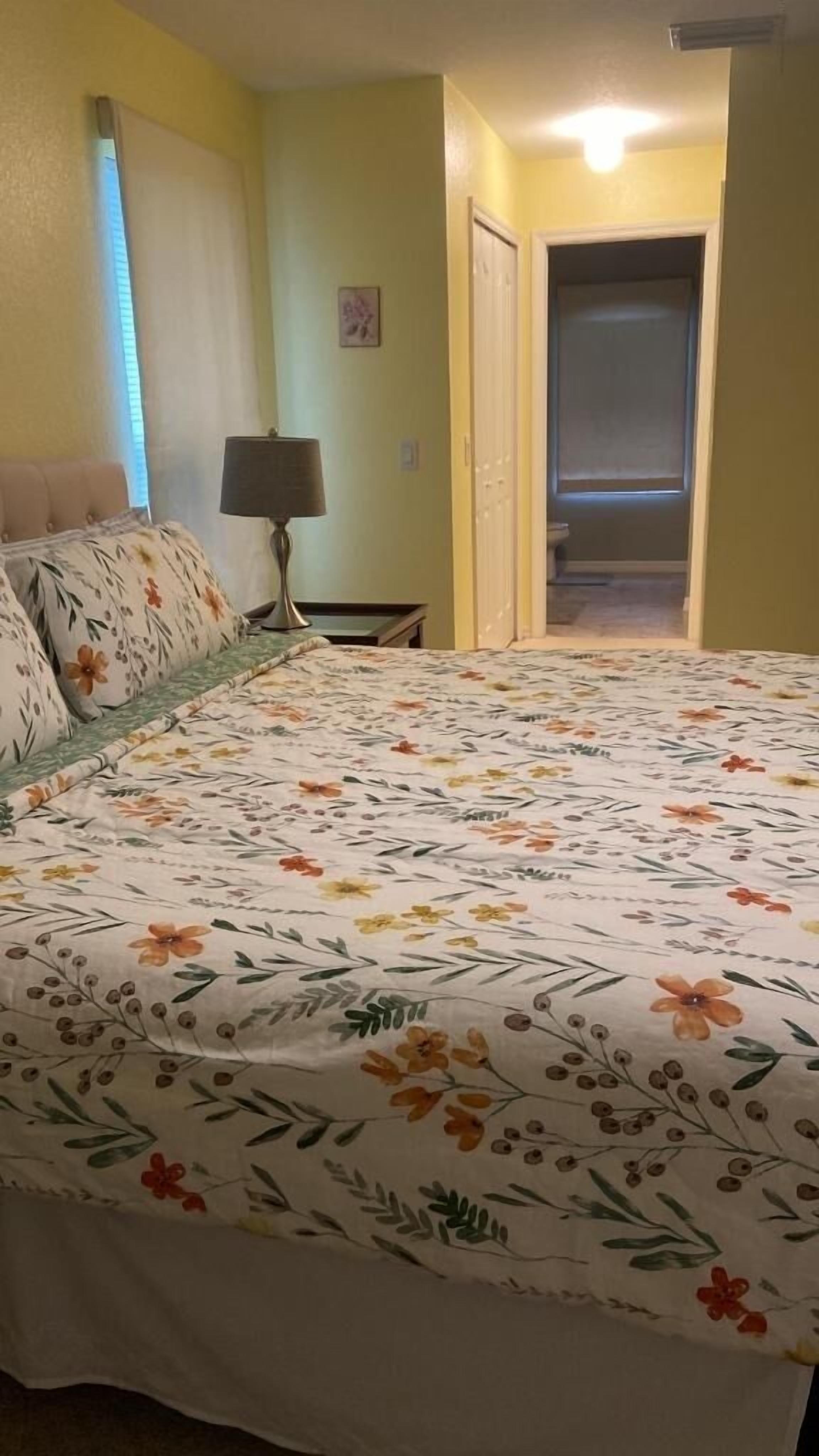 Una camera da letto con una coperta dal motivo floreale, una lampada da comodino e una porta che dà su un bagno.