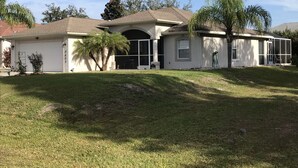 A two-story house with a garage, a covered patio, and a small front yard with a palm tree. - Quiet, Cozy, Bungalow with a Pool. Near Venice Beach and Warm Mineral Springs (North Port)