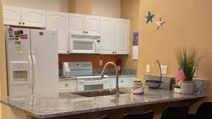 A kitchen with white cabinets, a granite countertop, a sink, and four black bar stools. - Quiet, Cozy, Bungalow with a Pool. Near Venice Beach and Warm Mineral Springs (North Port)