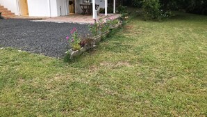 Uma casa com varanda coberta e um jardim com flores e uma pequena mesa.