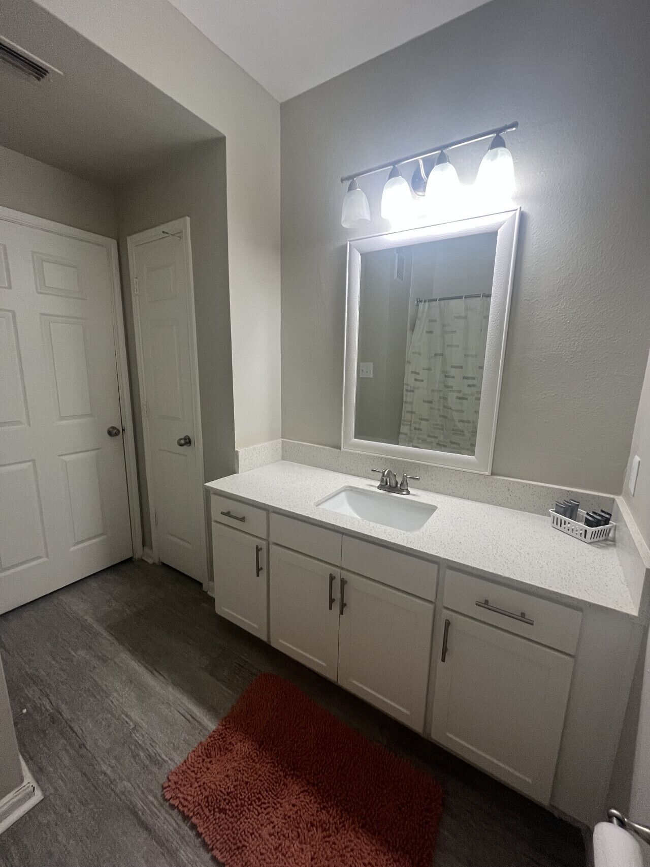 A bathroom with a white sink, a mirror with lights, and a red rug.